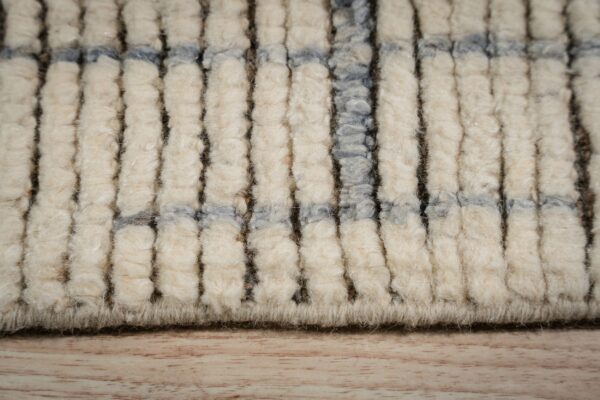 Extreme close-up showing thick, shaggy cream pile with dark vertical lines and intersecting blue bands on wood flooring.