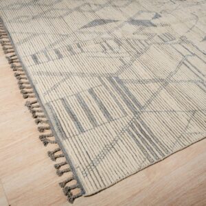 Cream textured rug with gray geometric lines and tassels lying on light wood-look panel flooring.