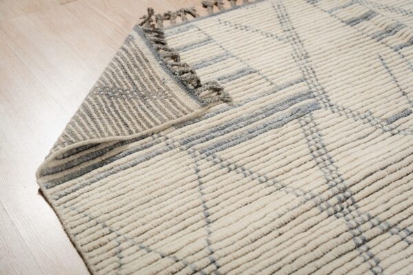 Textured cream rug with gray intersecting linear patterns and tassels on light wooden floor.