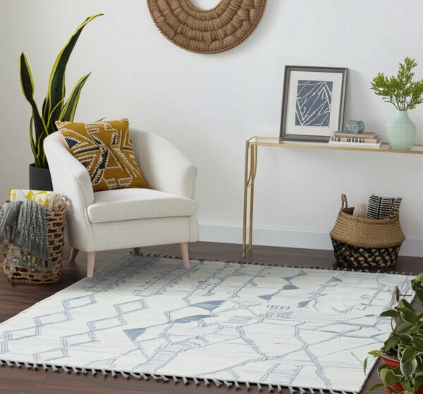 Cream and blue geometric low-pile rug with tassels grounds a sitting area with a white chair and wood floors.