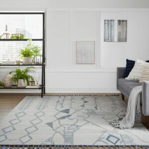 Light gray flatweave rug with a blue geometric pattern and tassels in a bright, modern living room.