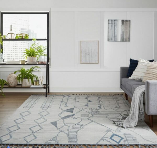 Light gray flatweave rug with a blue geometric pattern and tassels in a bright, modern living room.