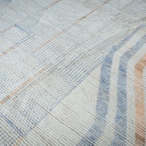 Textured, off-white rug with geometric stripes and grid patterns in soft blue and dusty peach.