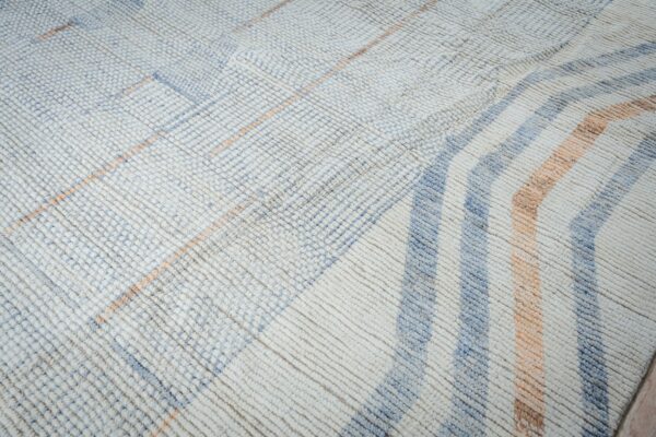 Textured, off-white rug with geometric stripes and grid patterns in soft blue and dusty peach.