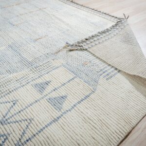Thick cream rug with blue geometric designs is folded back, showing the backing on light wood floor.