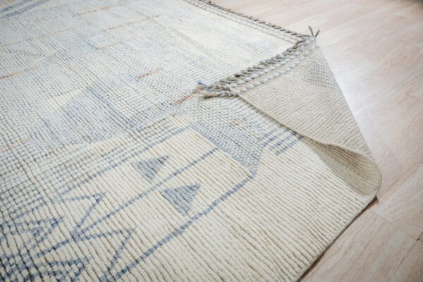 Thick cream rug with blue geometric designs is folded back, showing the backing on light wood floor.