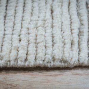 Off-white high pile rug featuring a thick, vertical corded texture rests upon light wood flooring.