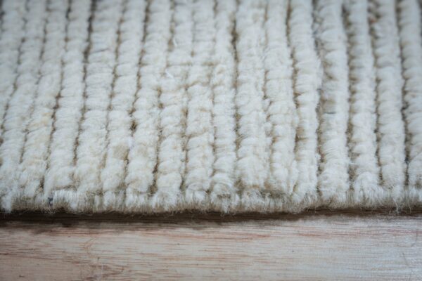 Off-white high pile rug featuring a thick, vertical corded texture rests upon light wood flooring.