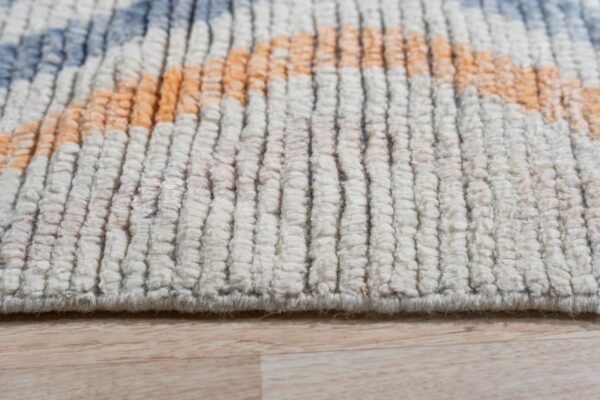 Thick, shaggy cream rug pile shows geometric orange and blue shapes over light wood.