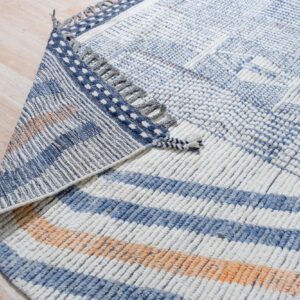 Chunky blue and white textured rug with orange accents folded over on pale wood plank flooring.