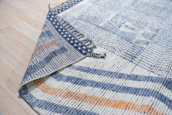 Chunky blue and white textured rug with orange accents folded over on pale wood plank flooring.