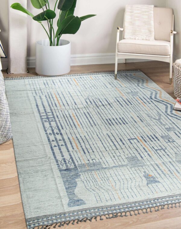 Light blue flatweave rug with abstract indigo and orange geometric lines sits on wood floor next to a white chair.