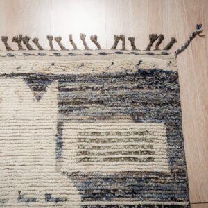 High pile, textured rug in cream and mixed blue-gray patterns, finished with knotted tassels on wood flooring.