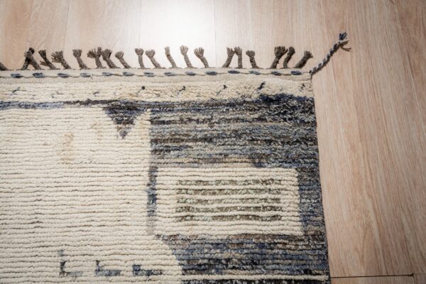 High pile, textured rug in cream and mixed blue-gray patterns, finished with knotted tassels on wood flooring.