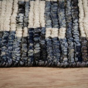 Close-up of chunky striped rug texture in cream, variegated blue, and brown resting on light wood flooring.