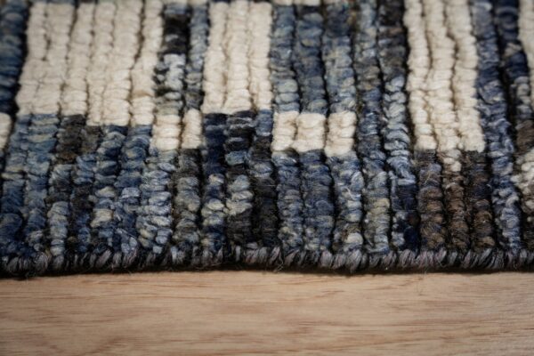 Close-up of chunky striped rug texture in cream, variegated blue, and brown resting on light wood flooring.