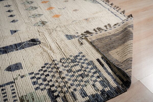 High-pile cream rug with blue and orange shapes folded over to expose the striped woven backing.