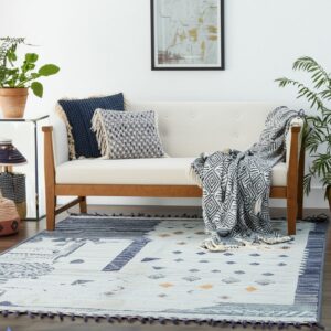 Light blue flatweave rug with navy geometric patterns and tassels beneath a modern wooden sofa.