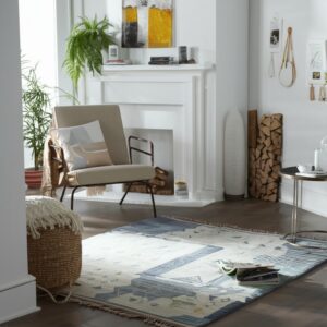 An abstract blue and cream rug anchors a reading nook with a beige chair by a white fireplace.
