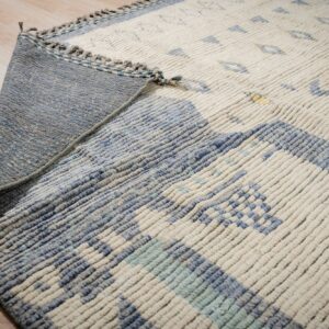 A high-pile cream and blue geometric rug is folded over, showing its flat woven blue backing.