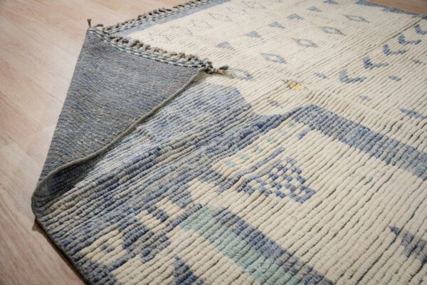 A high-pile cream and blue geometric rug is folded over, showing its flat woven blue backing.