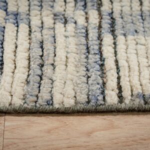 Detail shot of a plush, striped rug in shades of off-white, blue, and green, resting on wood floor.