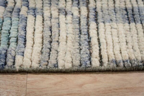 Detail shot of a plush, striped rug in shades of off-white, blue, and green, resting on wood floor.