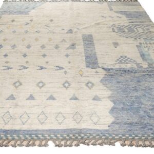 Abstract high-pile rug in cream and shades of blue with geometric elements and thick gray-taupe fringe.