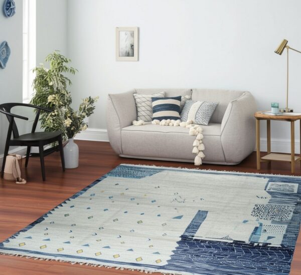 Abstract blue, gray, and yellow low-pile rug lying on wood flooring beneath a curved light sofa.