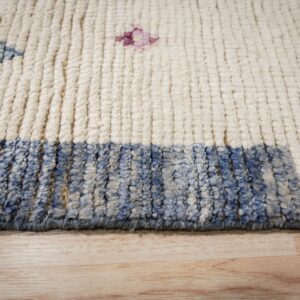 Detail of a high-pile cream rug with blue-mottled border and scattered geometric motifs on wood floor.