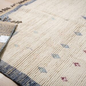 Thick cream rug with blue and magenta accents, showing ribbed texture and folded corner on wood floor.