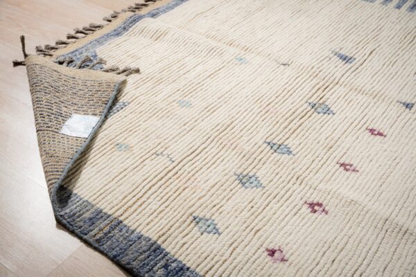 Thick cream rug with blue and magenta accents, showing ribbed texture and folded corner on wood floor.