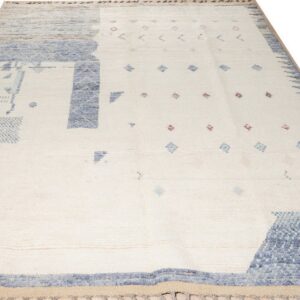 Shaggy cream rug with thick blue abstract patterns and small scattered pink and blue geometric accents.