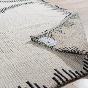 Close-up of a cream rug with black zigzag lines and a thick ribbed texture, folded over on a light wood floor.