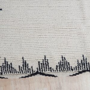 Off-white high-pile rug with a ribbed texture and black geometric patterns resting on light wood flooring.