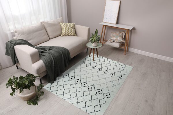 A cream rug with a black geometric diamond pattern sits on light wood flooring next to a beige sofa.