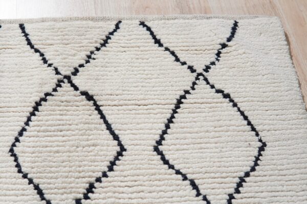High-pile cream rug with dark dotted geometric trellis lines rests on light wood floor.