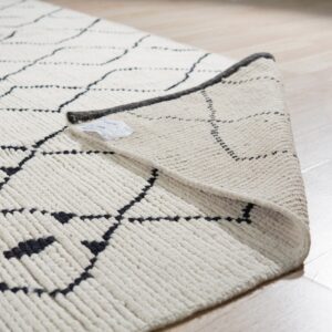 Close-up of a high-pile cream rug with black geometric lines folded over on light wood flooring.