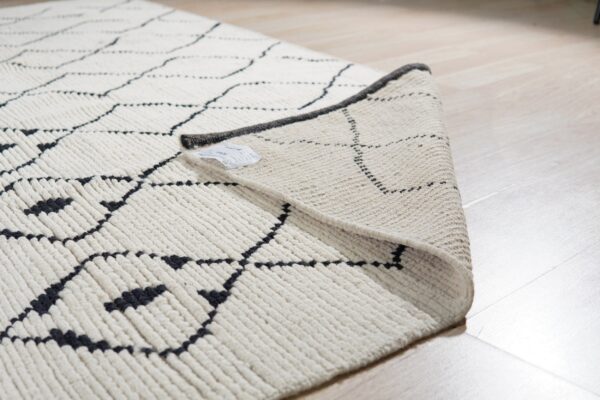 Close-up of a high-pile cream rug with black geometric lines folded over on light wood flooring.