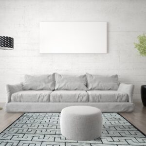 A geometric black and light blue patterned rug sits under a gray sofa and ottoman on wood flooring.