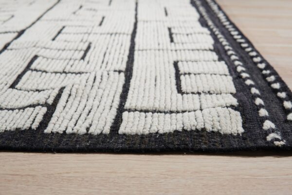 Textured charcoal and cream rug featuring a blocky geometric pattern on light wood floor.
