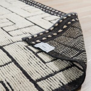 Cream and dark gray geometric rug texture, high pile, with the edge folded over on light wood flooring.