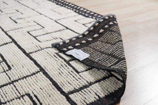 Cream and dark gray geometric rug texture, high pile, with the edge folded over on light wood flooring.