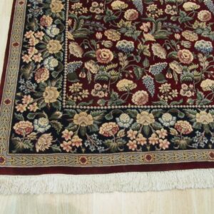 Maroon rug with a dense multicolored floral design and contrasting dark navy border on light wood flooring.