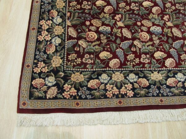 Maroon rug with a dense multicolored floral design and contrasting dark navy border on light wood flooring.