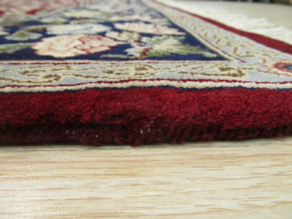 A thick, deep red pile rug with a traditional floral pattern rests on light blonde wood flooring.