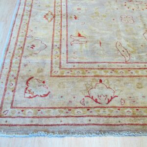Low pile beige rug with distressed red floral motifs and multiple borders over light wood flooring.