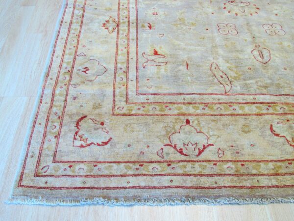 Low pile beige rug with distressed red floral motifs and multiple borders over light wood flooring.