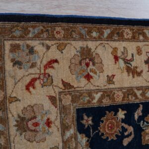 Close-up of a floral rug showing the navy field and detailed beige and brown multi-border design on wood planks.