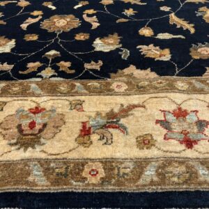 Navy blue high-pile rug with tan floral motifs and a detailed beige border on a light wood floor.